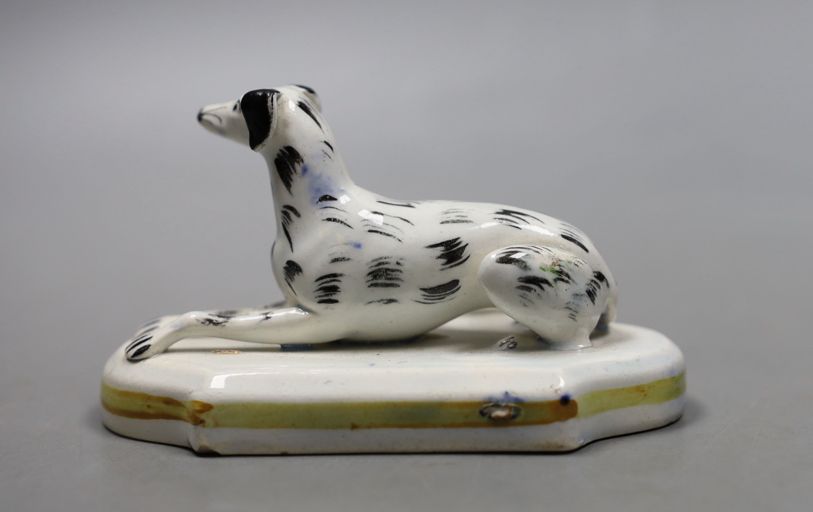 A Staffordshire porcelain model of a recumbent greyhound, c.1830–50, with black markings to its fur, 10.2 cm long, Provenance- Dennis G Rice collection